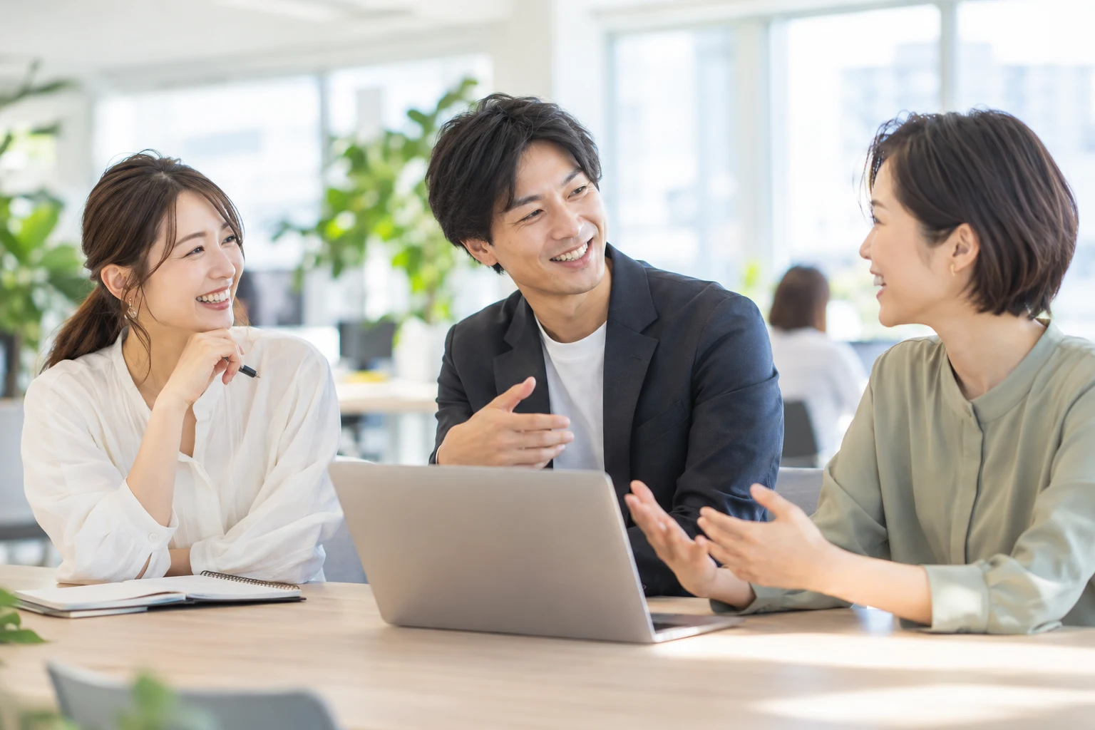 明るい職場で、笑顔で会話する3人の社員のイメージ
